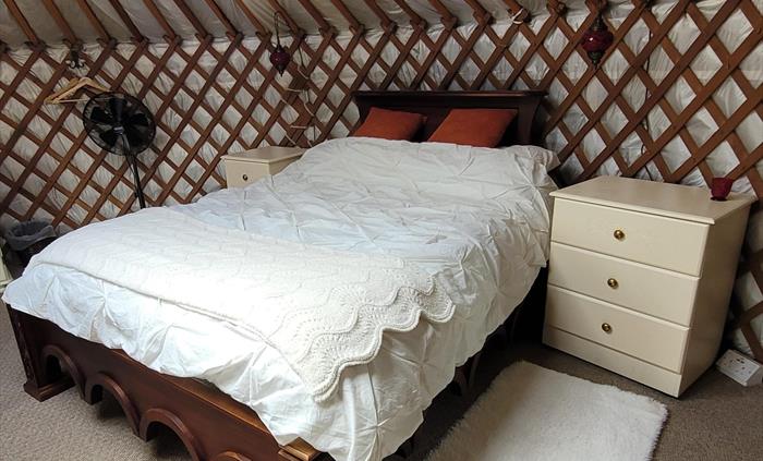 Carved dark wood bed with intricate base details and cream cotton pintuck bedding, cream blanket and burnt orange velvet cushions. Cream painted drawe